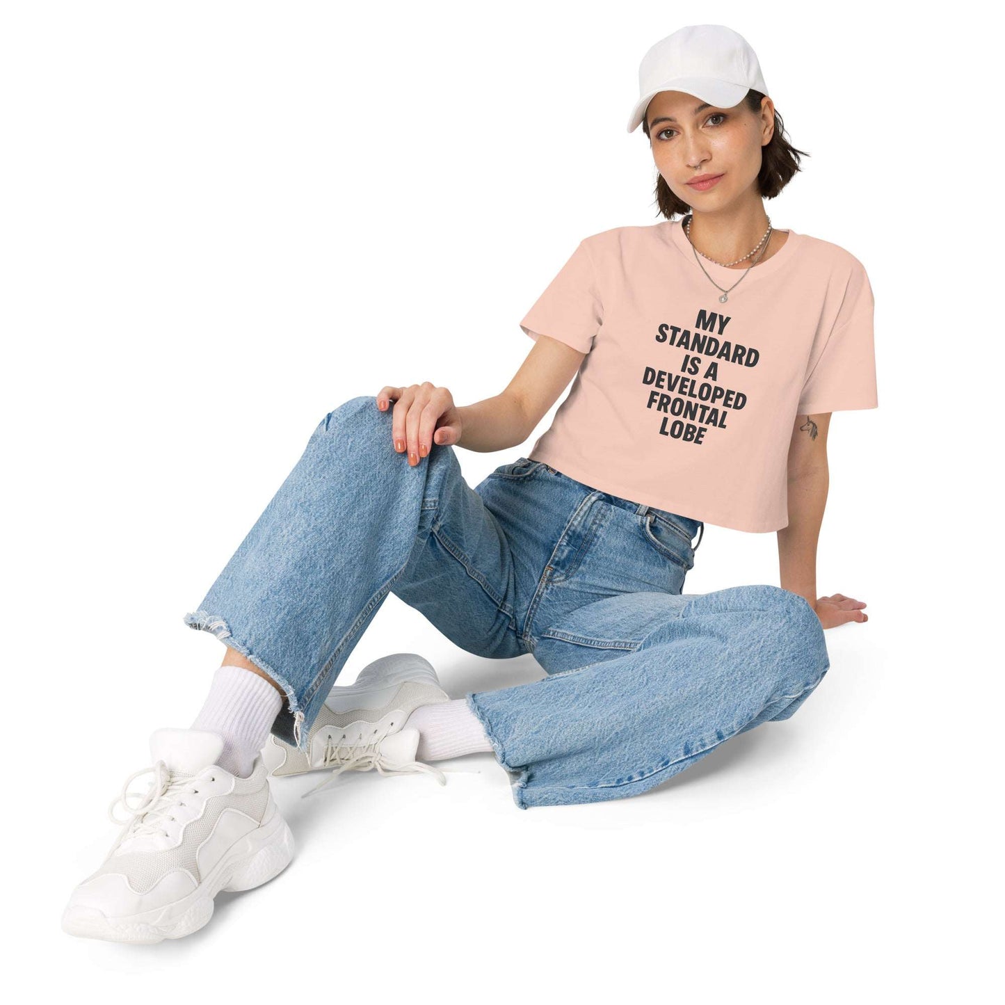 Person wearing a pink t-shirt with text and blue jeans sitting on a white background