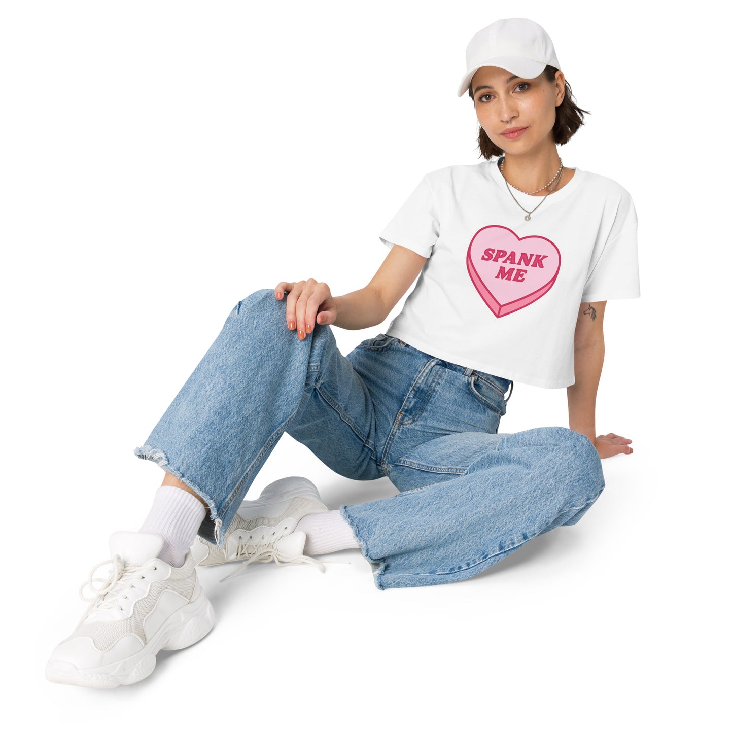 Person wearing a white t-shirt with a colorful heart design, blue jeans, and white sneakers on a white background